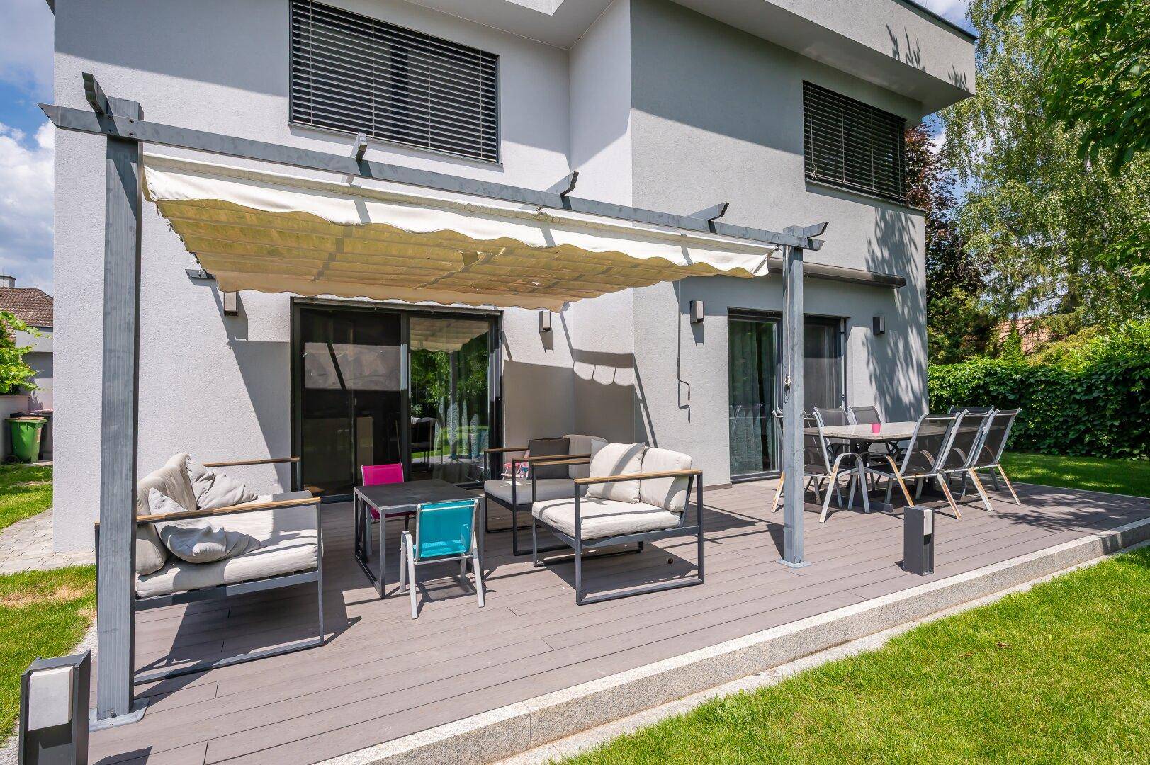 Moderne Terrasse mit bequemen Lounge-Möbeln und Esstisch, geschützt durch eine Pergola.