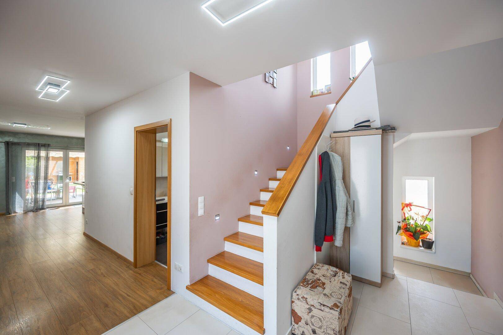 Heller Eingangsbereich mit Holztreppe, Fliesenboden und Garderobe, offen zum Wohnbereich.