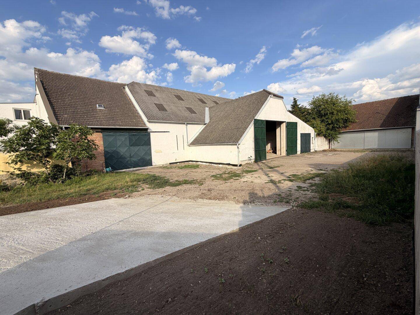Gesamtansicht des Gebäudekomplexes mit einem neu gepflasterten Bereich und einem großen Dach.