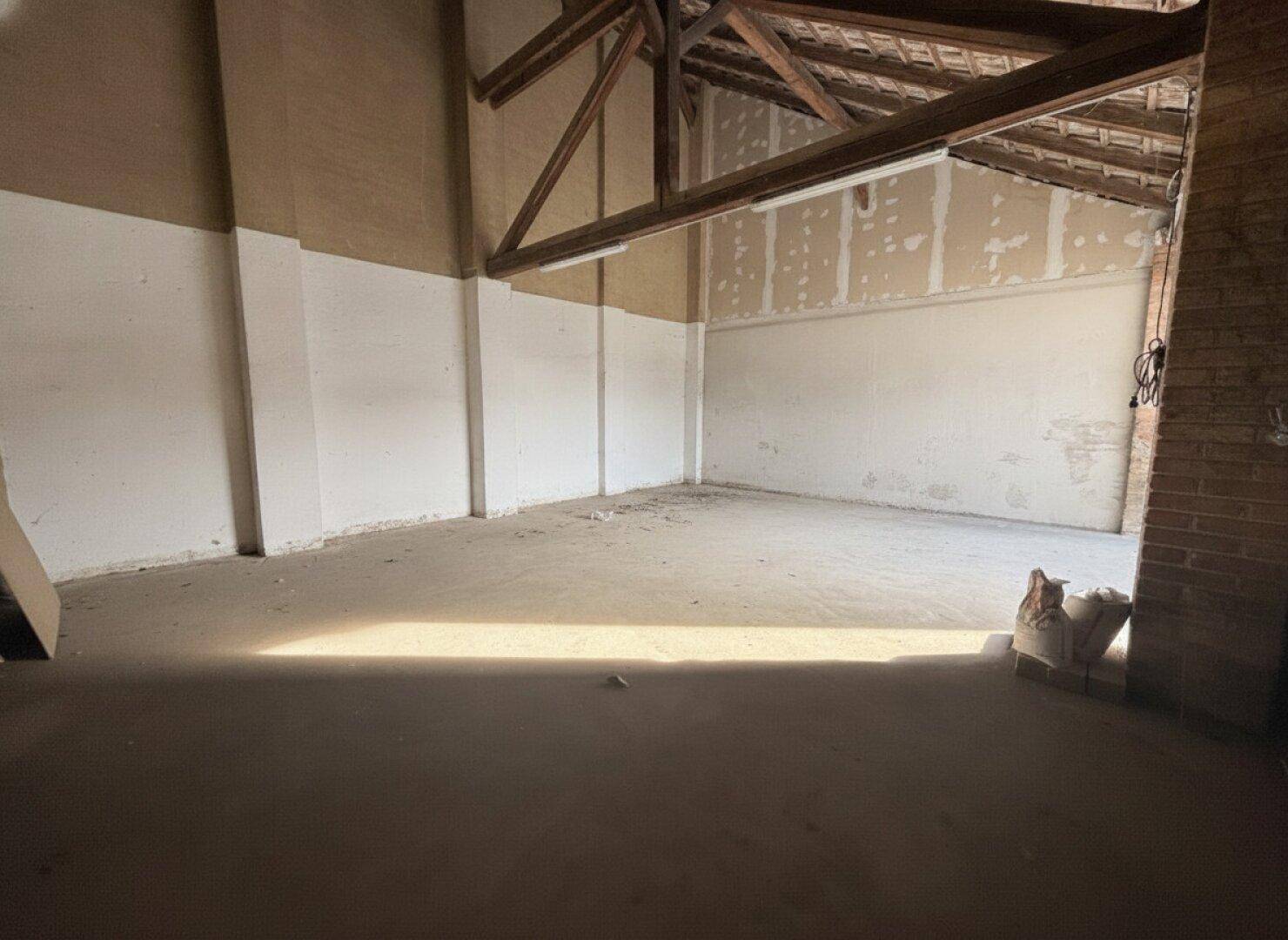 Rohbau eines Raumes mit sichtbaren Holzbalken und teilweise verputzten Wänden, bereit für den Ausbau.