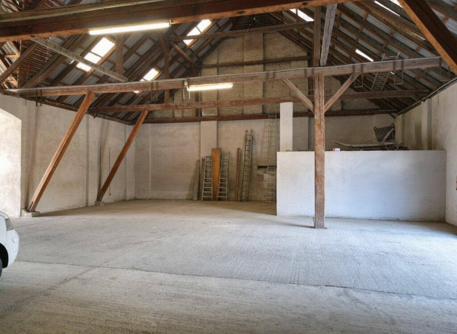 Großer, offener Lagerraum mit sichtbaren Holzbalken und einem Betonboden unter dem Dach.