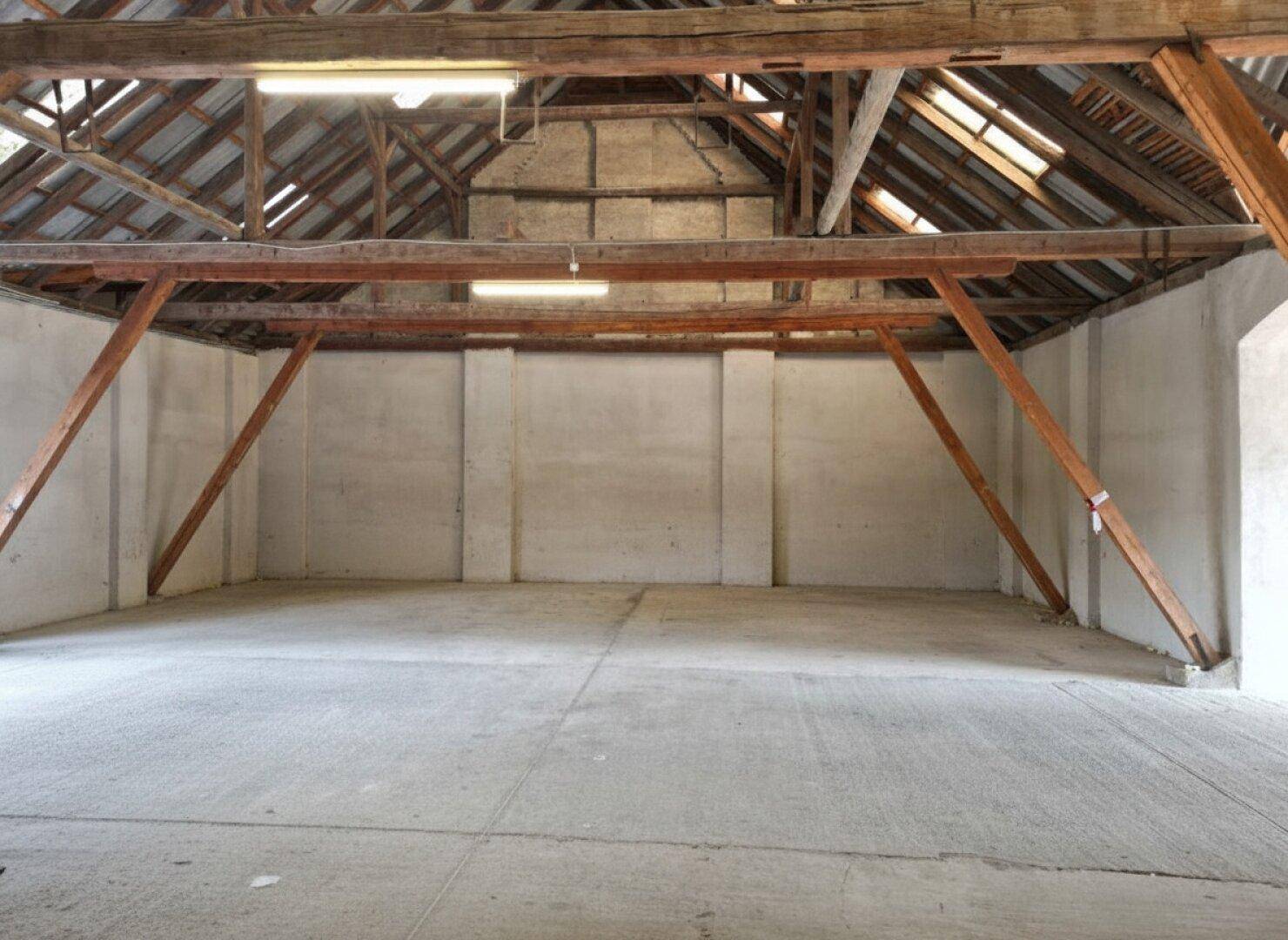 Geräumiger Innenraum mit freiliegenden Holzbalken und einem robusten Betonboden, ideal für Lagerzwecke.