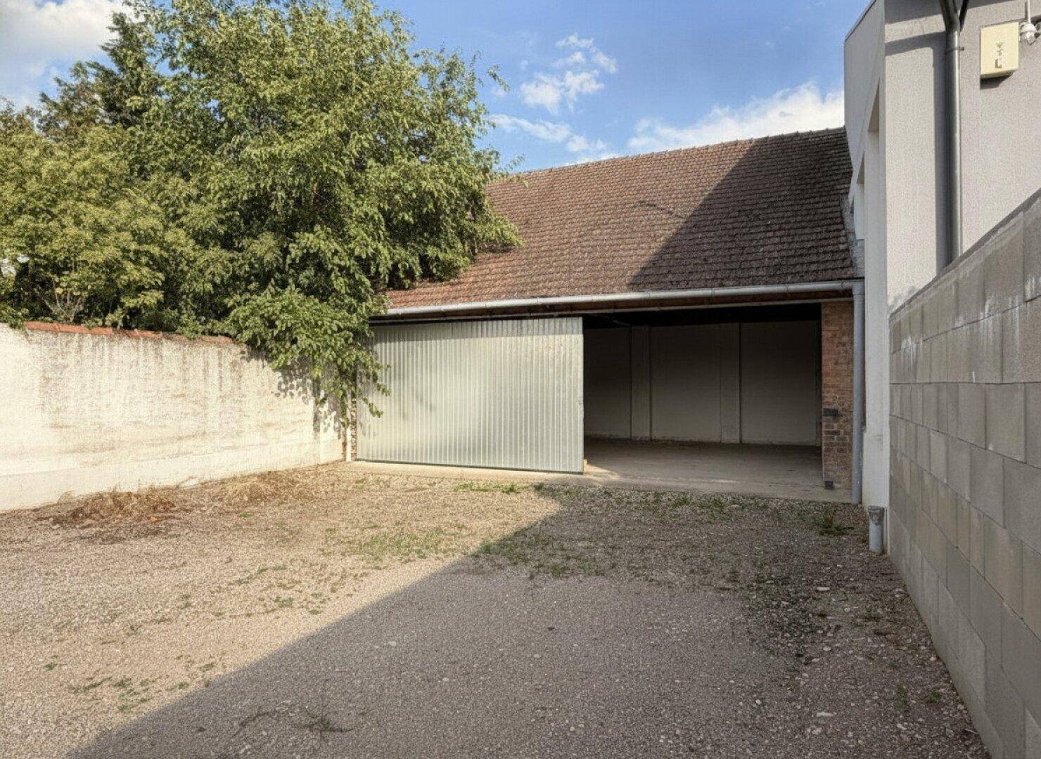 Außenansicht eines Schuppens oder einer Garage mit einem großen Wellblechtor und einem Schotterbereich.