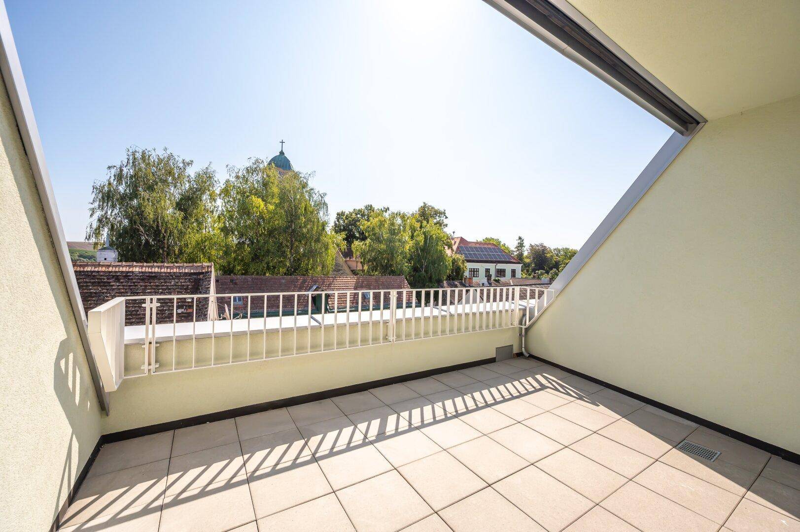 Großer, sonniger Balkon mit Fliesenboden und weitem Blick über die Dächer der Stadt in einem Neubau.