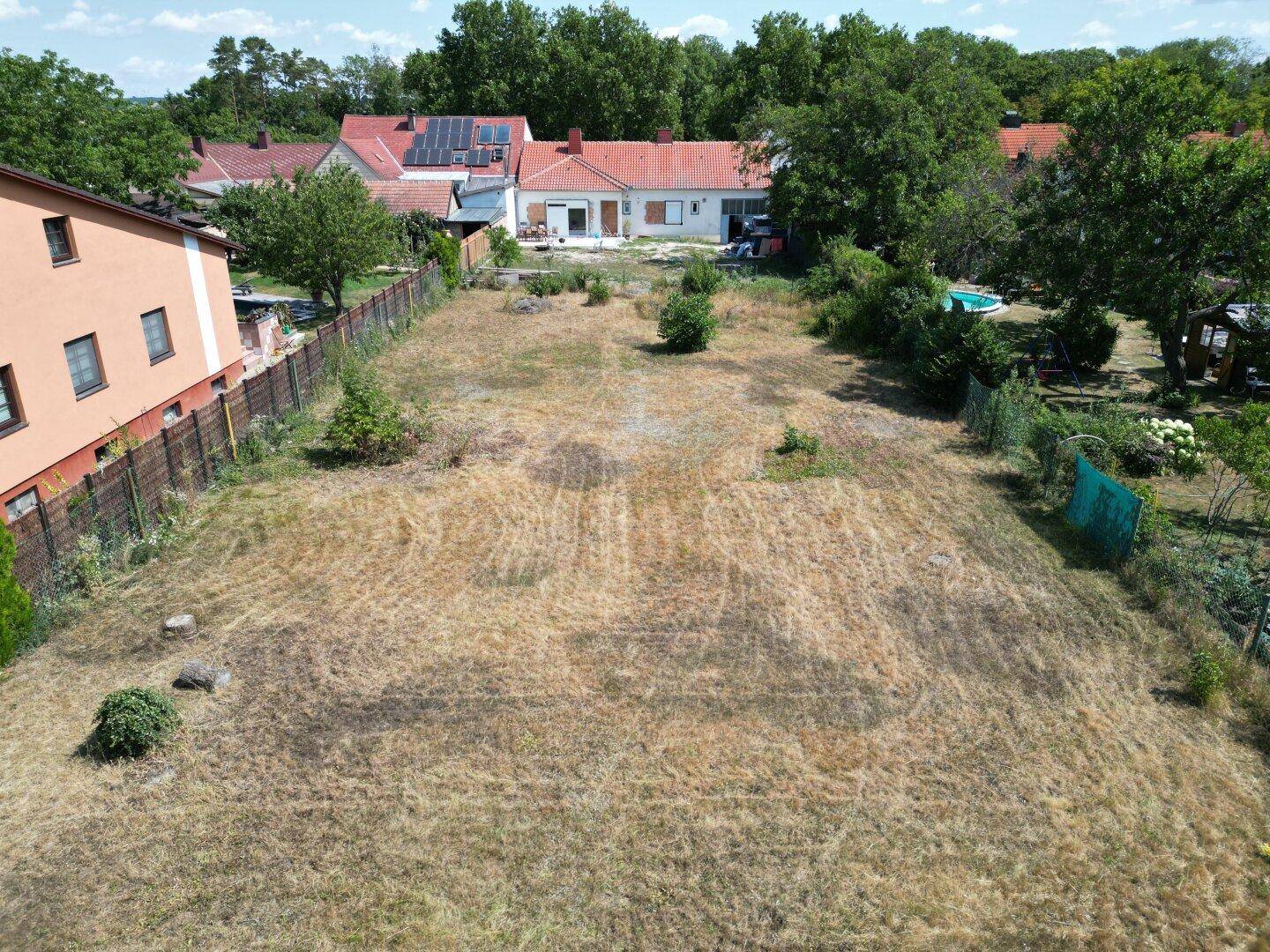Luftaufnahme eines weitläufigen Grundstücks mit trockenem Gras und angrenzenden Gärten.