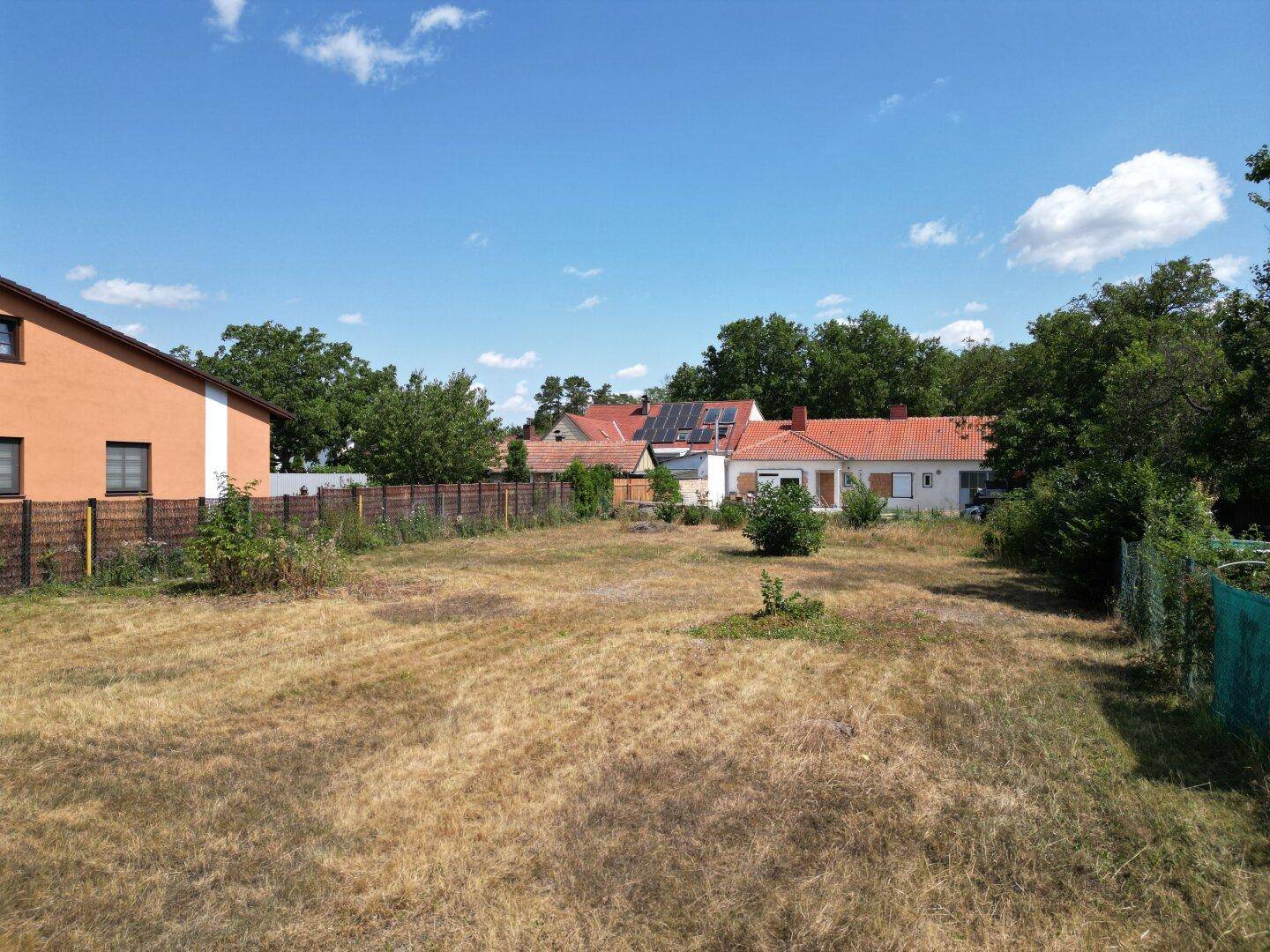Sonniger Blick über ein trockenes Grundstück mit angrenzenden Häusern und Zäunen.