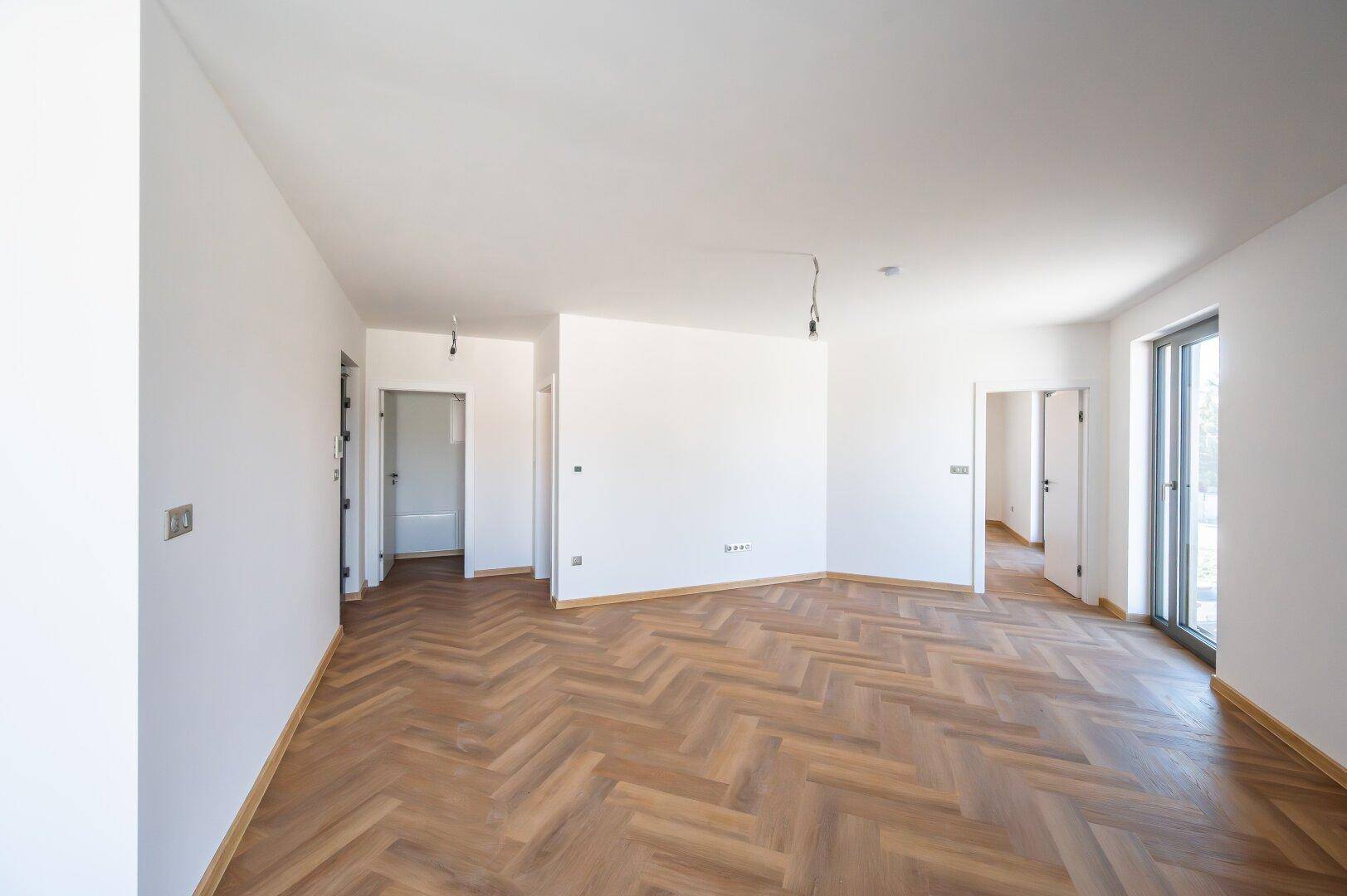 Geräumiges, helles Wohnzimmer mit Fischgrätparkett und Zugang zu weiteren Räumen.