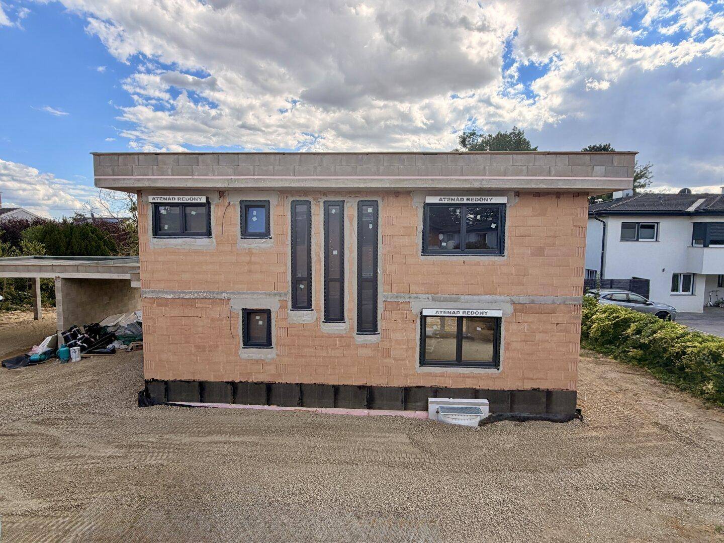 Vorderansicht eines modernen Neubaus in Massivbauweise mit unterschiedlichen Fensterformaten.