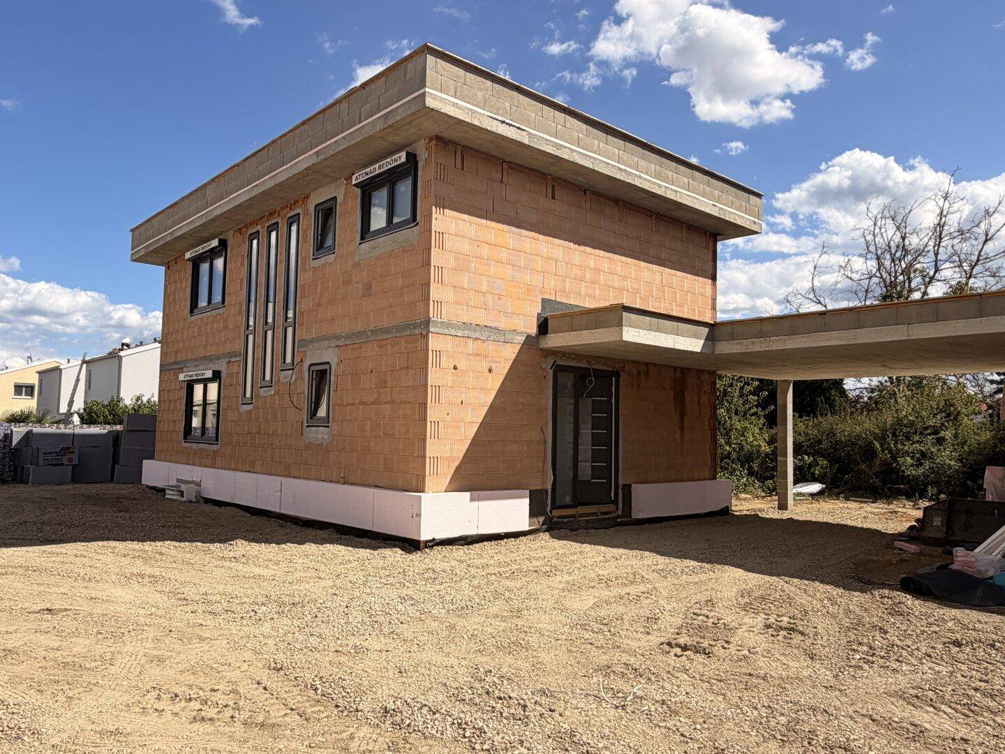 Ansicht des Rohbaus eines modernen Einfamilienhauses mit Carport-Vorbereitung und Flachdach.