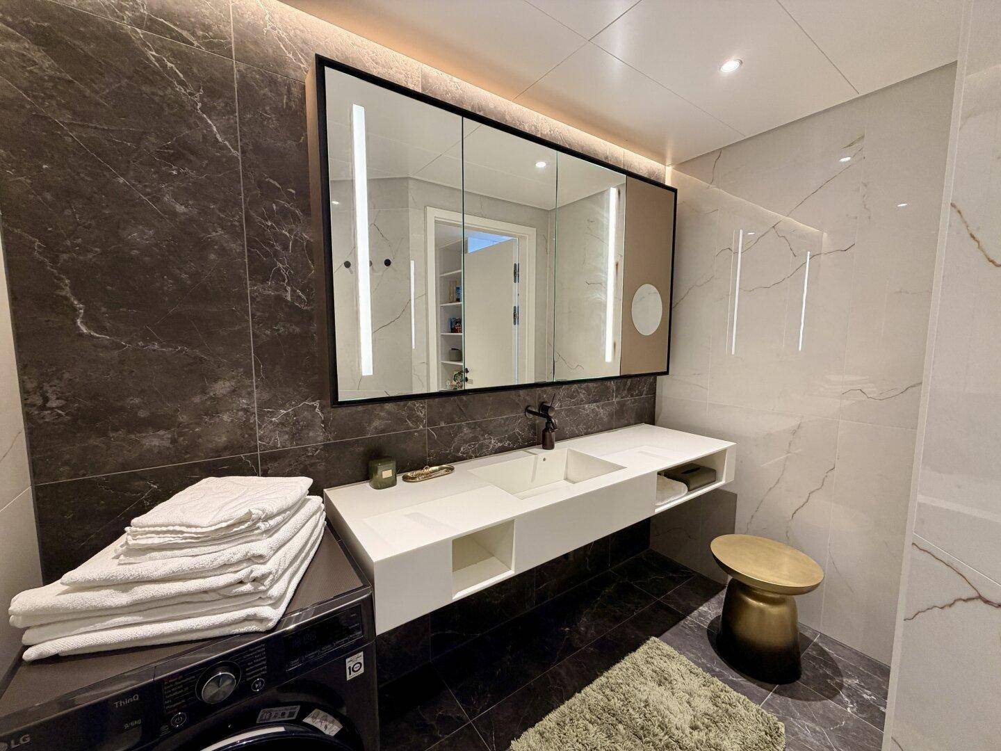 Elegantes Badezimmer mit Doppelwaschbecken, großem Spiegelschrank und integrierter Waschmaschine.