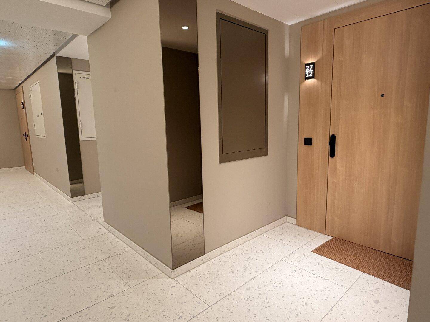 Eingangsbereich einer Wohnung mit Holztür und modernem Fliesenboden im Mehrfamilienhaus.