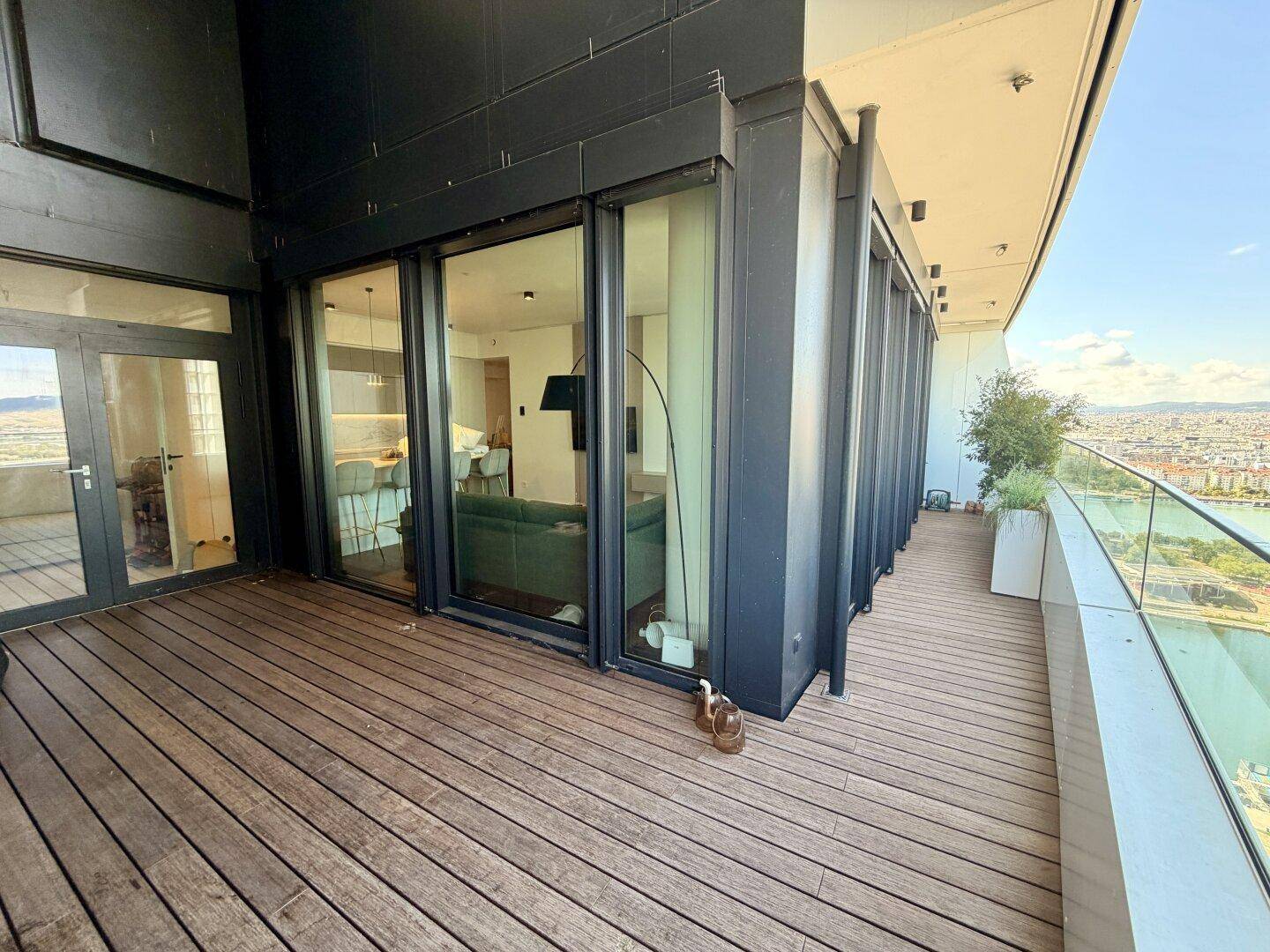 Geräumiger Balkon mit Holzboden und Glasgeländer, bietet weiten Blick auf die Umgebung.