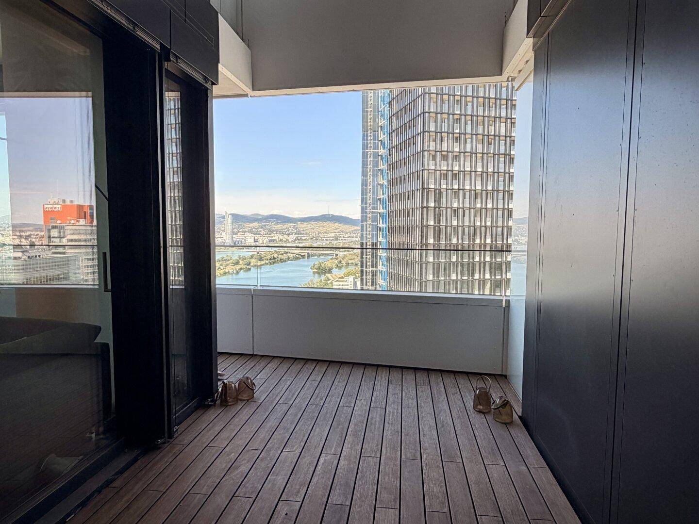 Balkon mit Holzboden und Blick auf moderne Hochhäuser und die Donau.