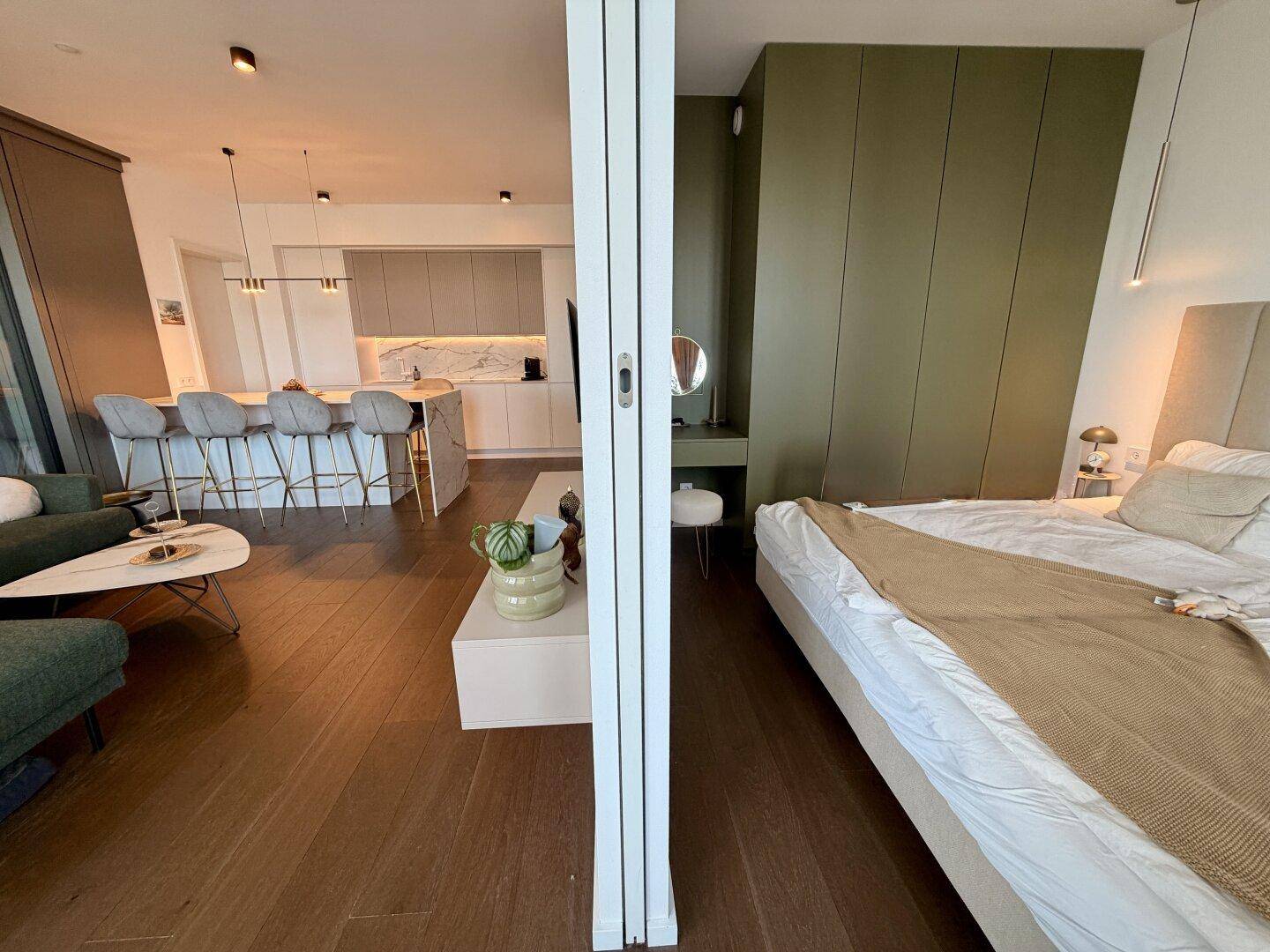 Offener Wohnbereich mit Küche und angrenzendem Schlafzimmer, getrennt durch eine Falttür.