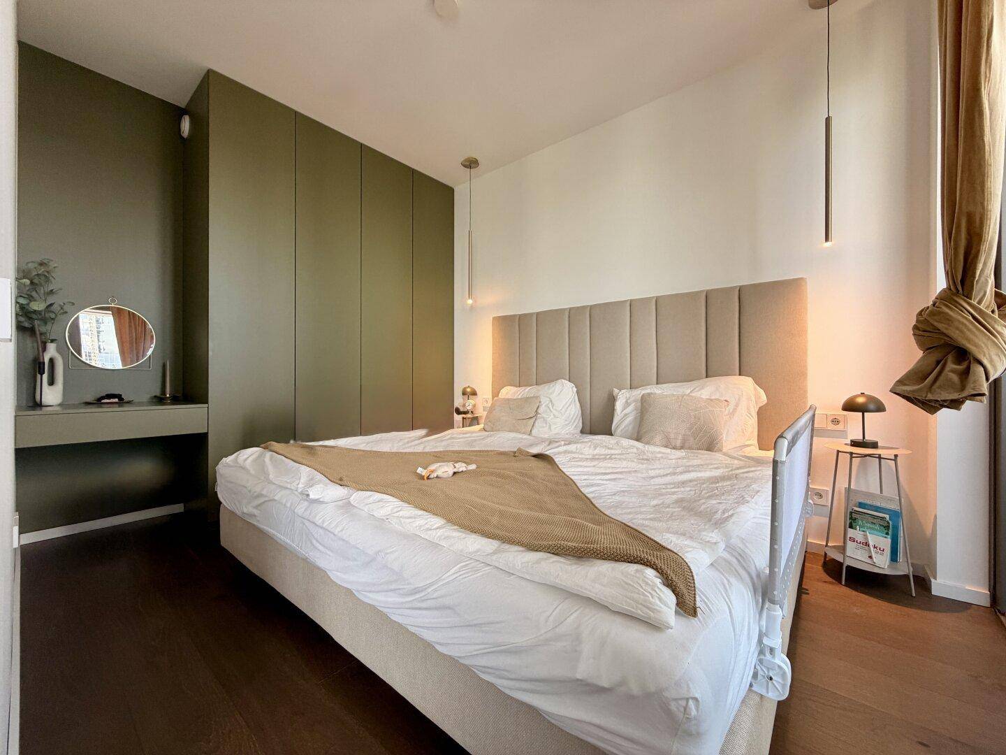 Modernes Schlafzimmer mit großem Bett, grünen Einbauschränken und stilvoller Beleuchtung.