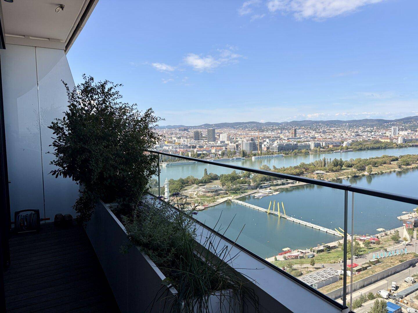 Balkon mit Pflanzenkübeln, Glasgeländer und beeindruckendem Panoramablick über die Stadt und den Fluss.