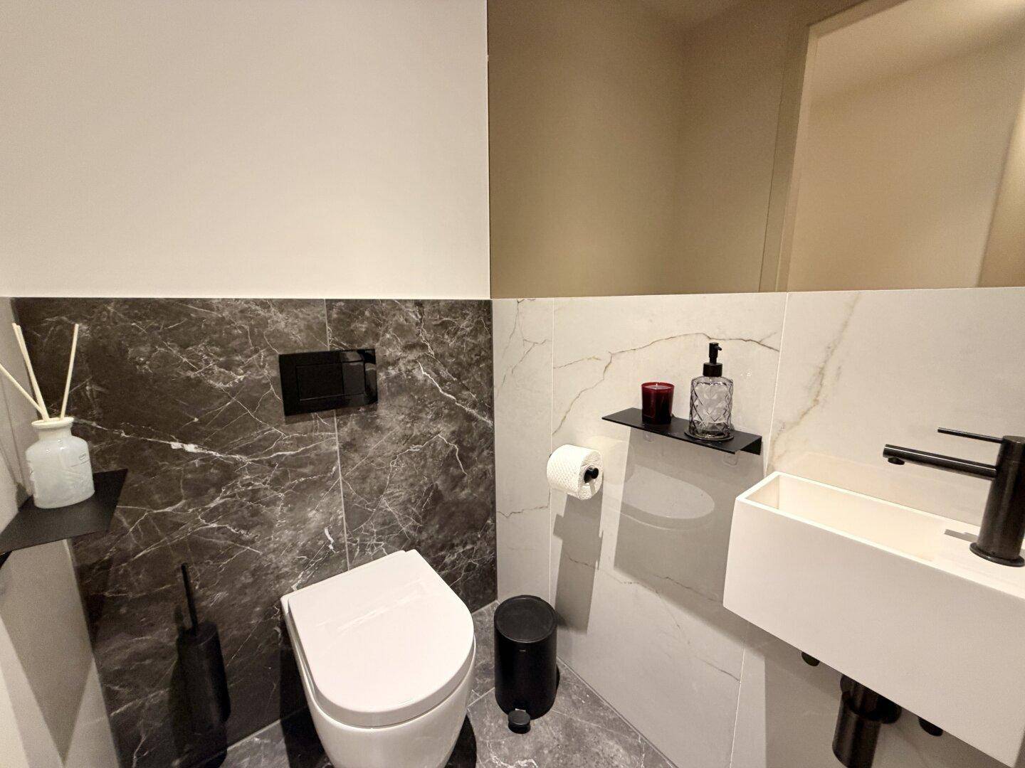 Modernes Gäste-WC mit dunklen Marmorfliesen, wandhängendem WC und stilvollem Waschbecken.