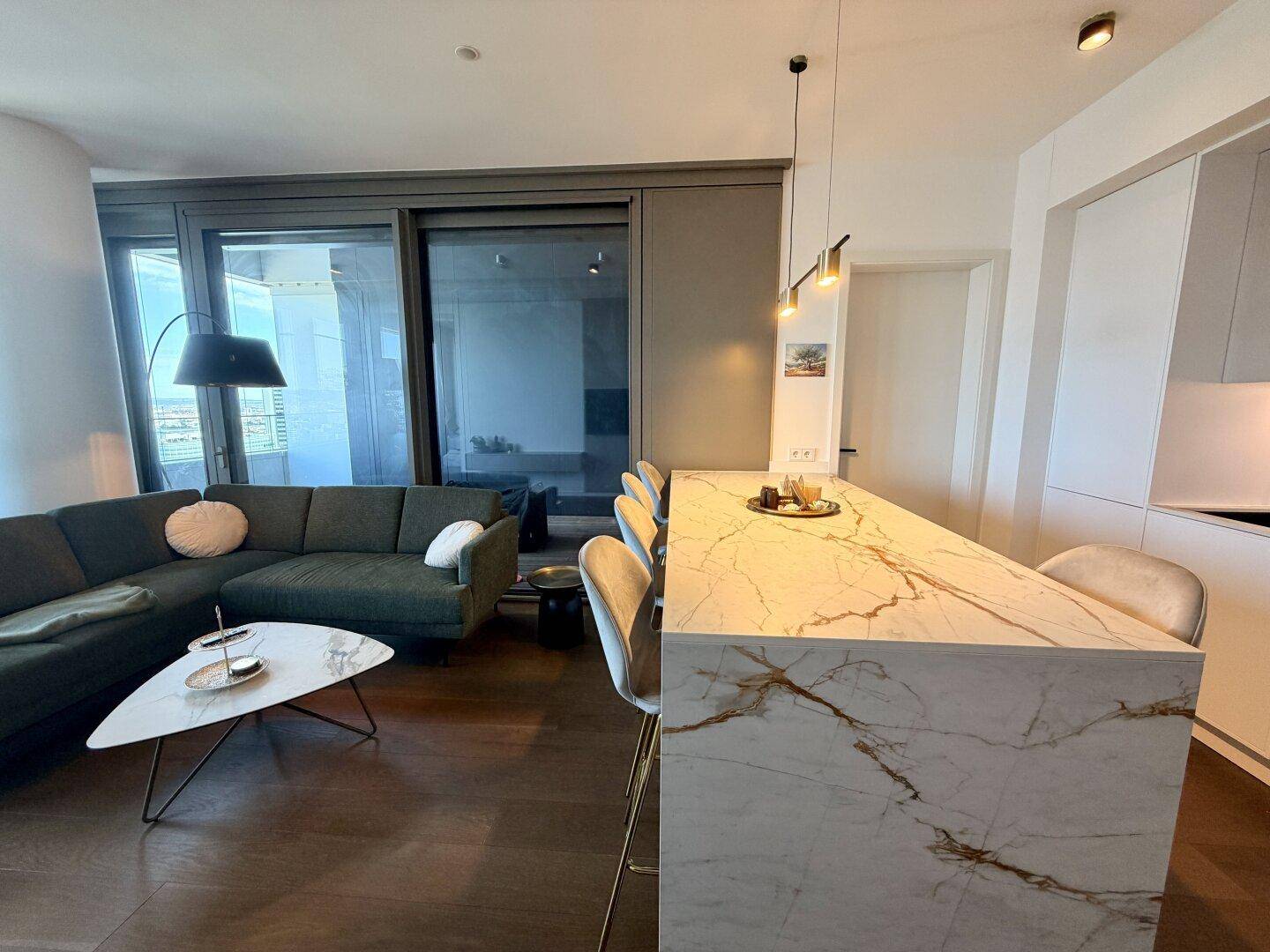 Offener Wohnbereich mit Kücheninsel, bequemer Couch und großen Fenstern mit Ausblick.