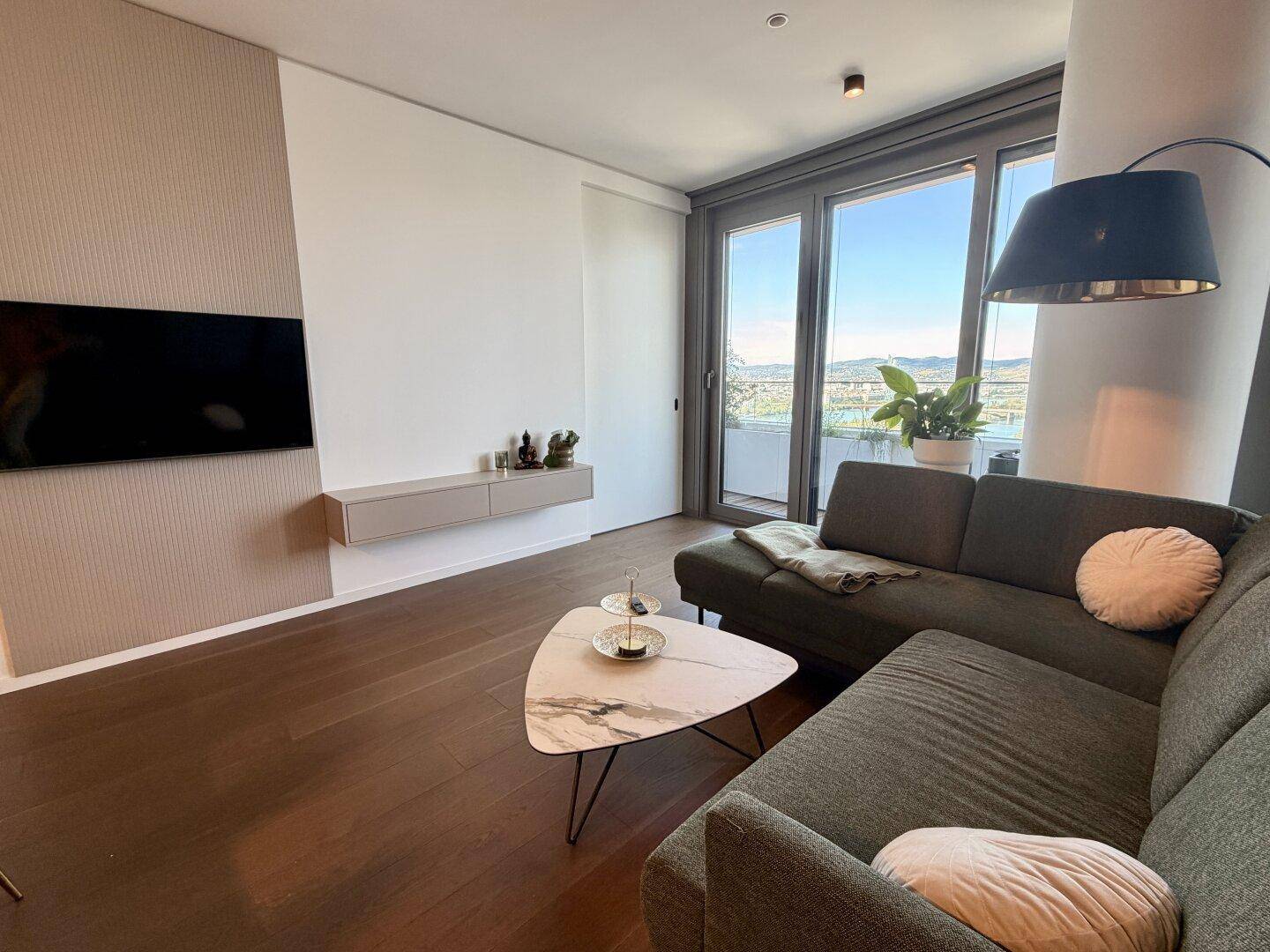 Gemütliches Wohnzimmer mit bequemer Couch, Holzboden und Zugang zu einem Balkon.