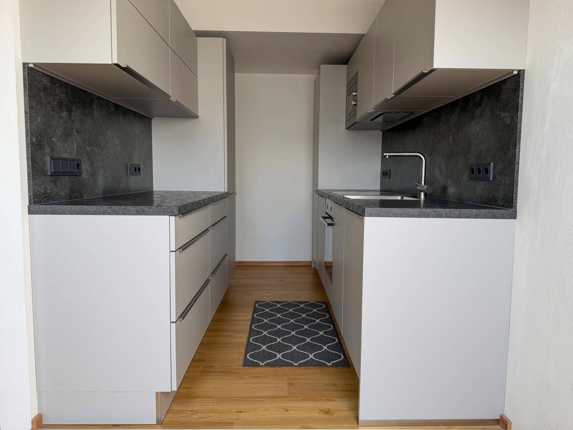 Moderne Küche mit hellgrauen Schränken, dunklen Arbeitsplatten und Holzfußboden in einem schmalen Raum.