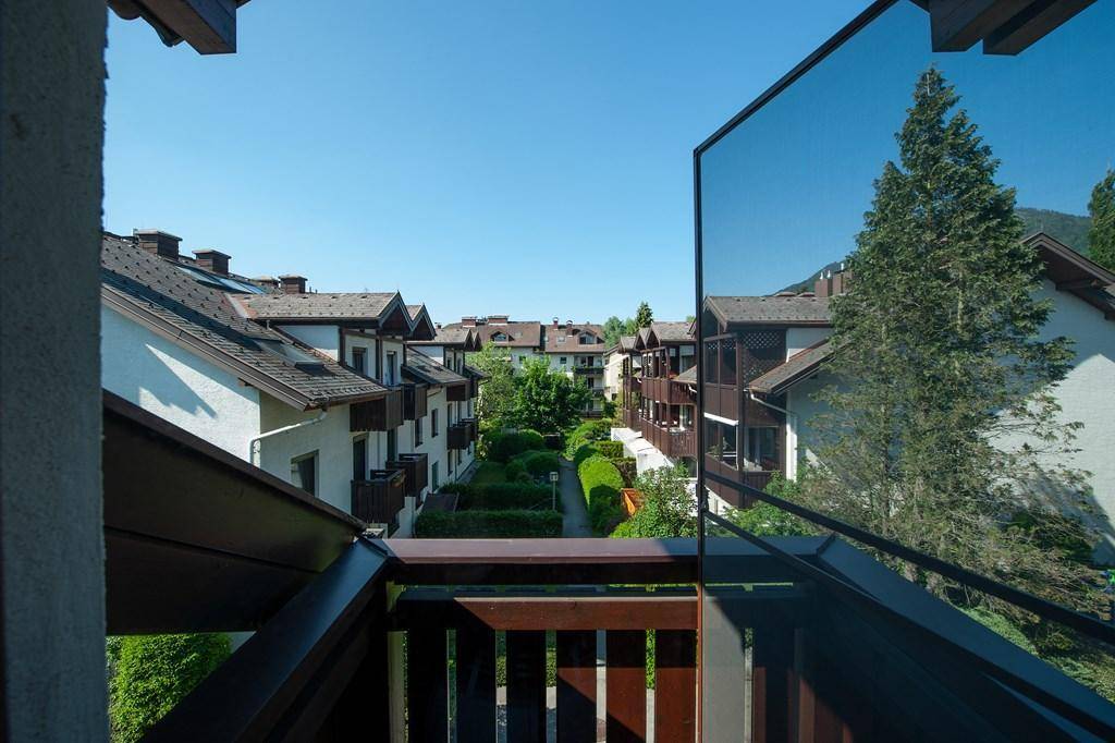 Blick von einem Balkon auf eine gepflegte Wohnanlage mit viel Grün und klarem blauem Himmel.