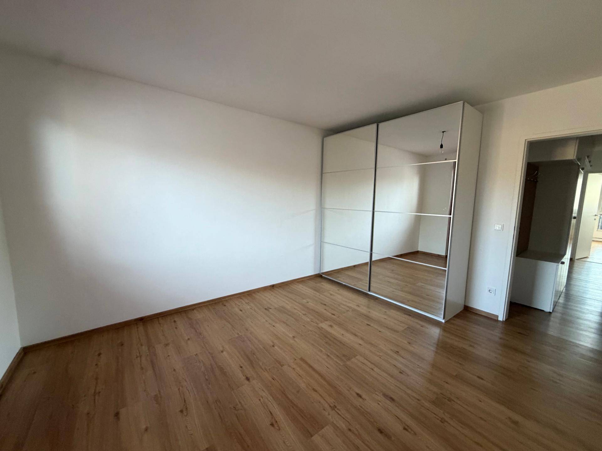 Helles Schlafzimmer mit Holzfußboden und einem großen Spiegelschrank, der den Raum optisch vergrößert.