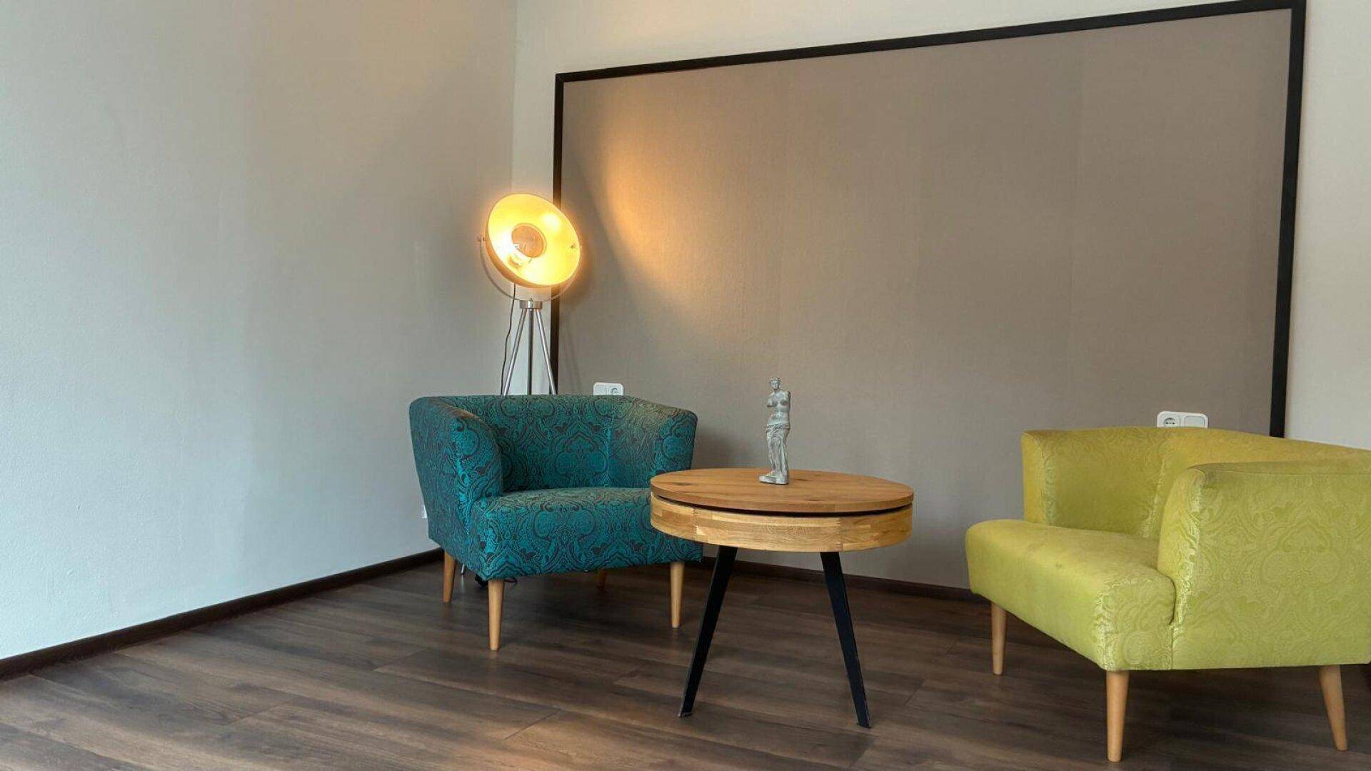 Gemütlicher Wohnbereich mit farbigen Sesseln, Holztisch und einer modernen Stehlampe.