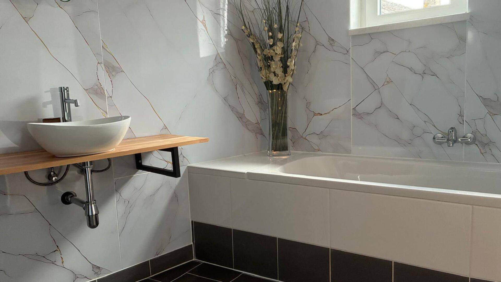 Helles Badezimmer mit Badewanne, modernem Waschbecken und Marmoroptik-Wandfliesen.