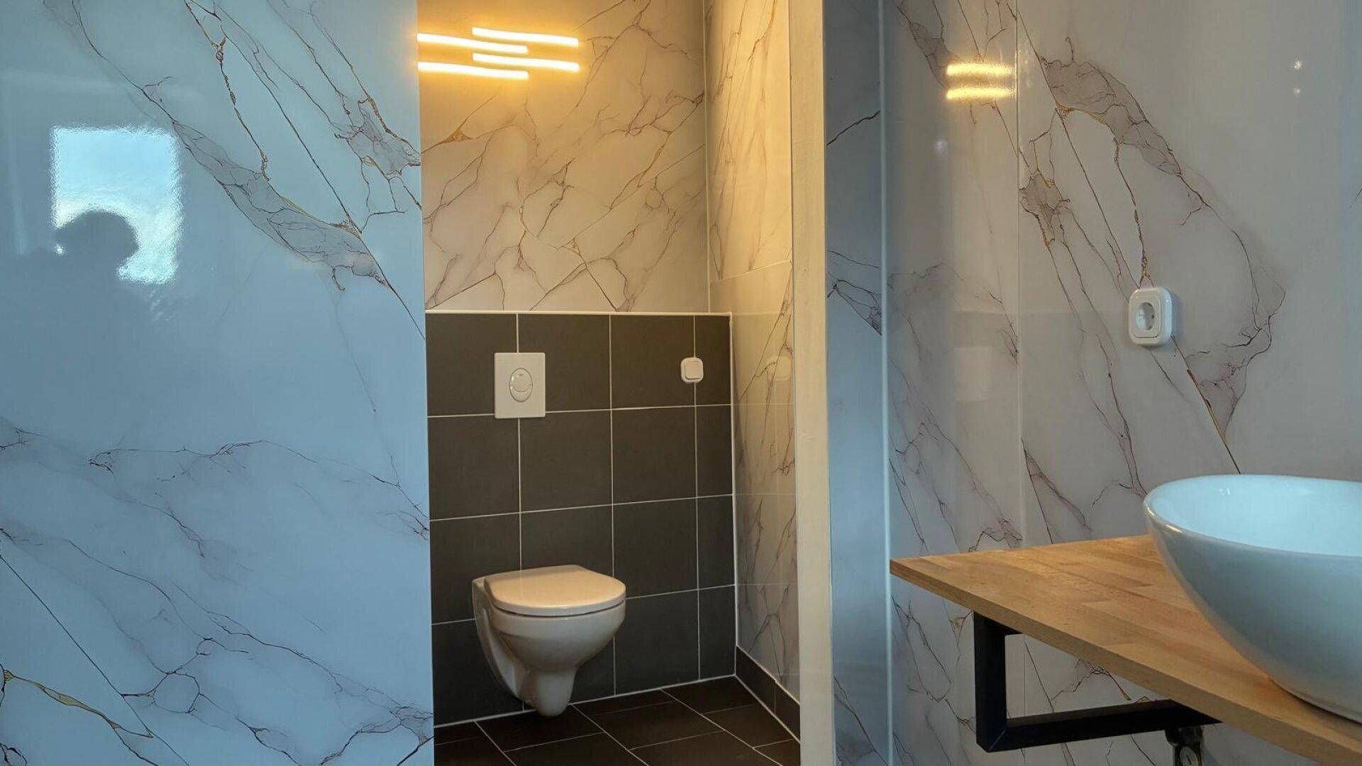 Modernes WC mit Marmoroptik-Fliesen, Wand-WC und stilvoller Beleuchtung.