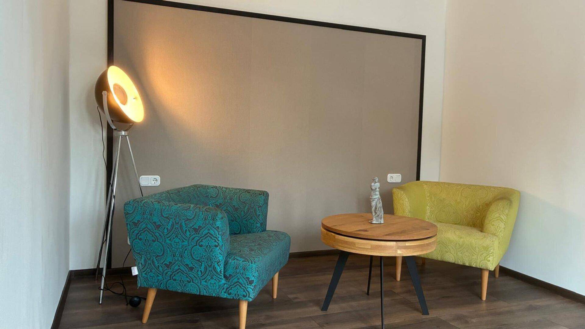 Gemütlicher Wohnbereich mit farbigen Sesseln, Holztisch und einer modernen Stehlampe.