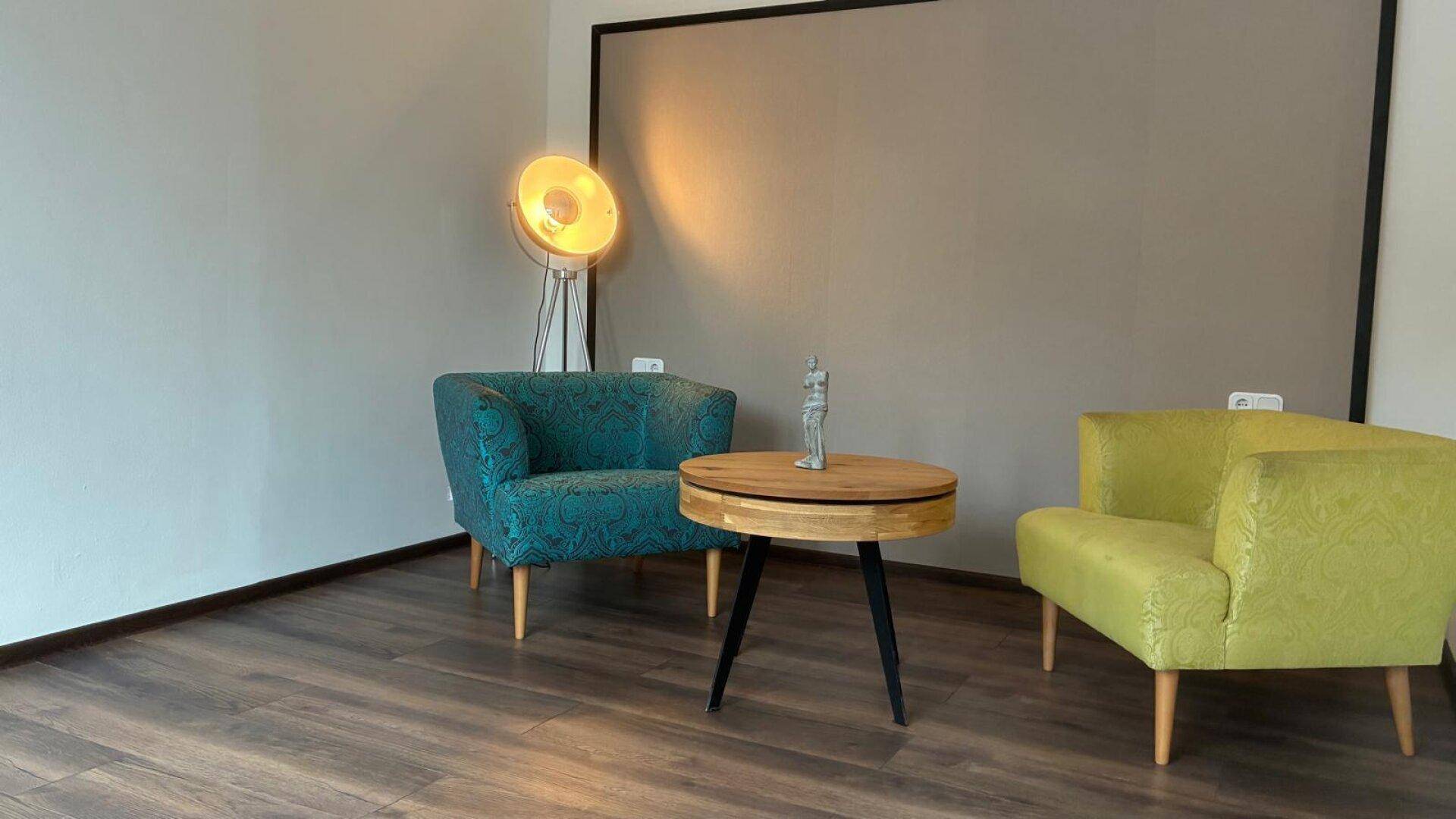 Gemütlicher Wohnbereich mit farbigen Sesseln, Holztisch und einer modernen Stehlampe.