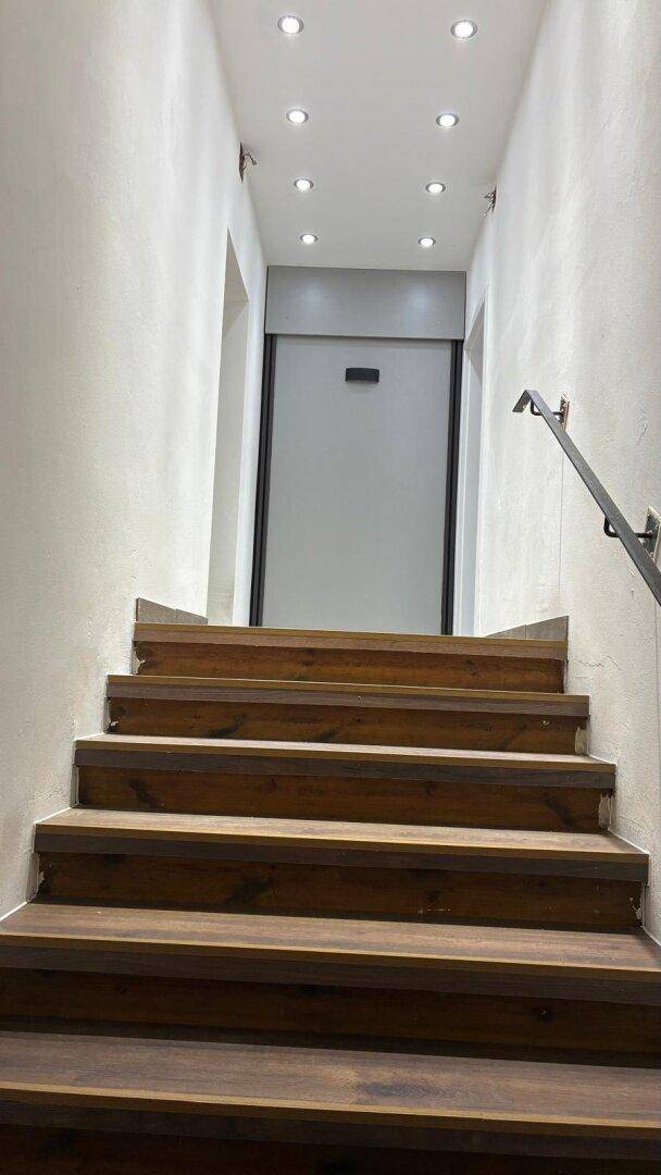 Moderner Treppenaufgang mit Holzstufen, Handlauf und integrierter Deckenbeleuchtung.