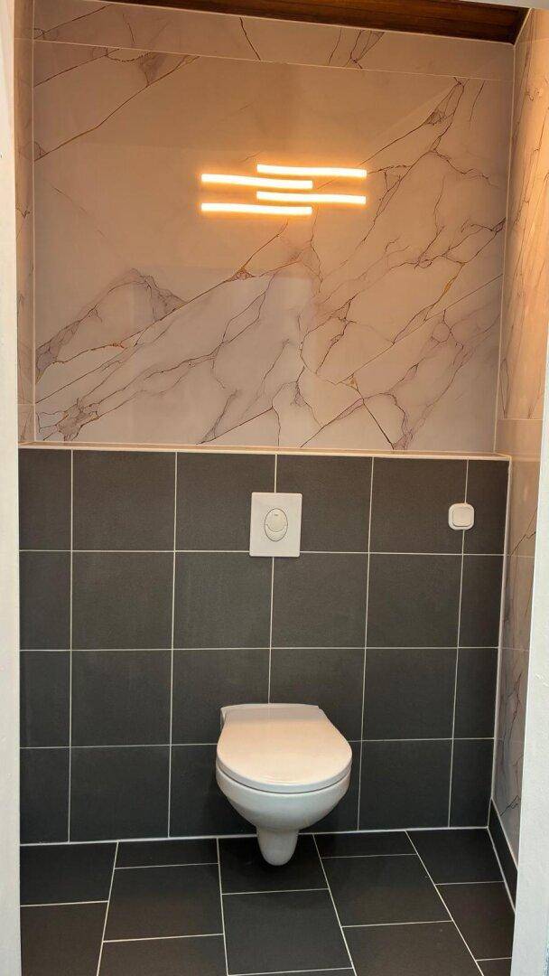 Modernes Wand-WC mit dunklen Fliesen und Marmoroptik-Wandverkleidung.