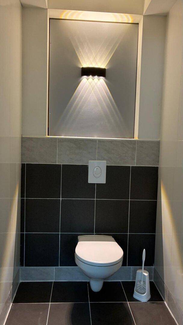Modernes Wand-WC mit dunklen Fliesen und indirekter Beleuchtung an der Wand.
