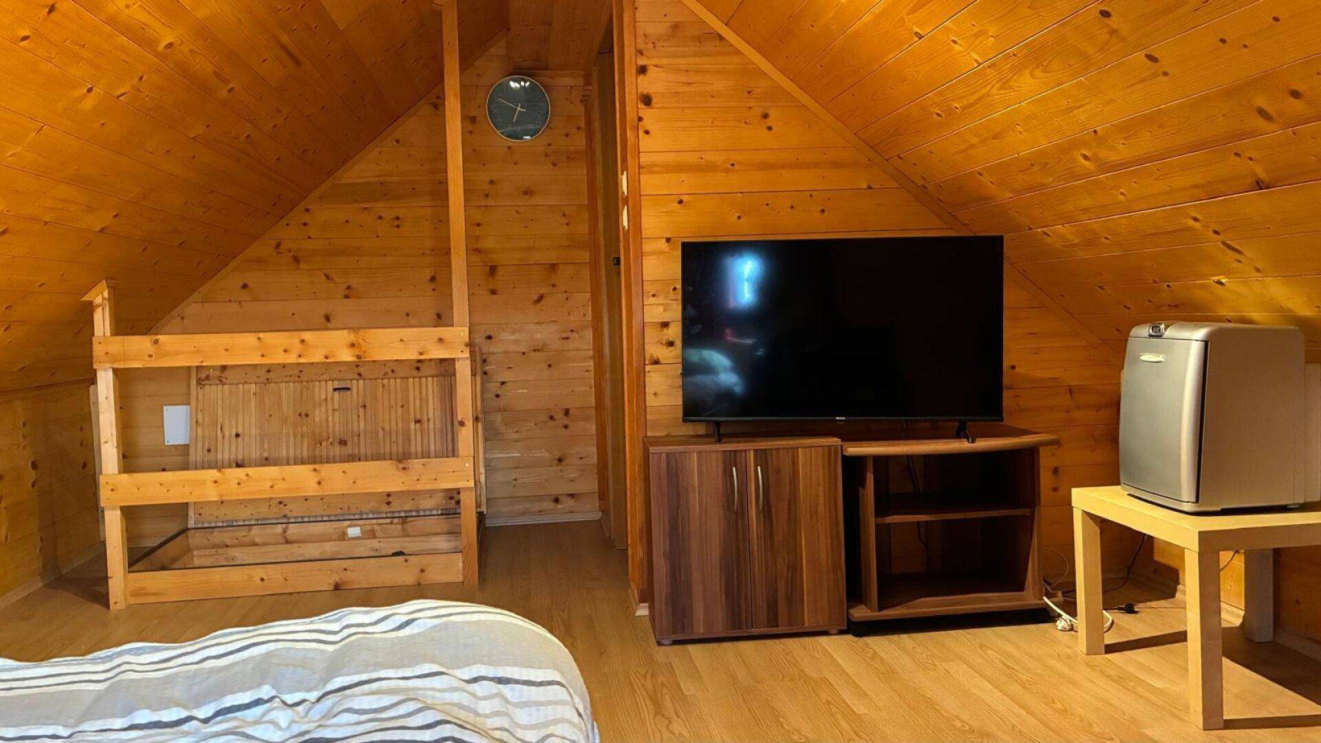 Dachgeschoss-Schlafzimmer mit Holzwänden, Fernseher und einem kleinen Kühlschrank.