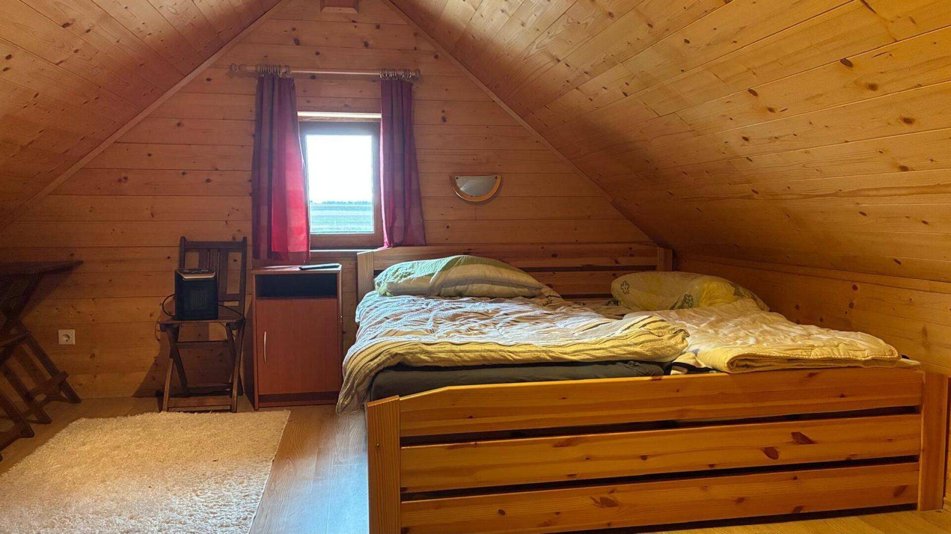 Helles Schlafzimmer im Dachgeschoss mit Holzbett und Blick ins Grüne durch das Fenster.