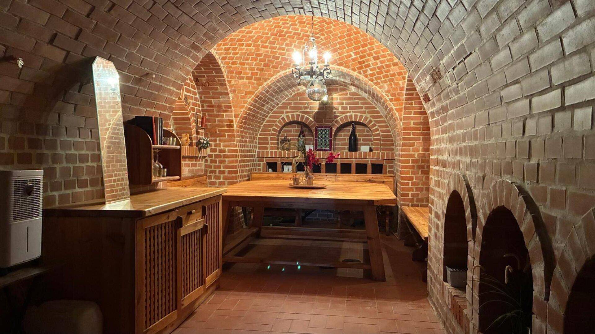 Rustikaler Weinkeller mit Ziegelgewölbe, großem Holztisch und traditioneller Einrichtung.