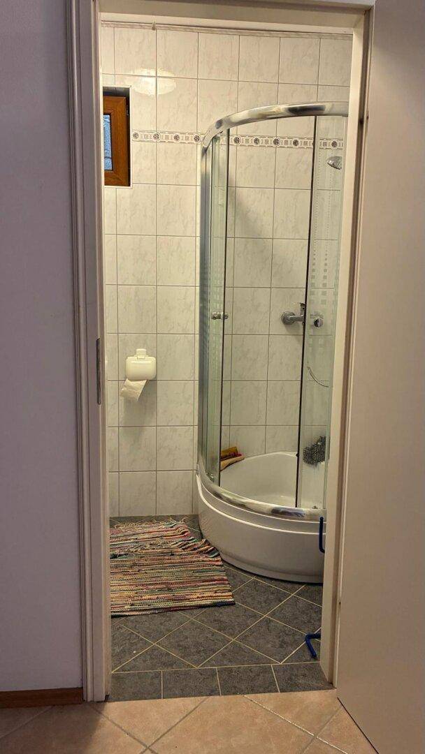 Badezimmer mit Duschkabine, Fliesenboden und Fenster für ausreichend Tageslicht.
