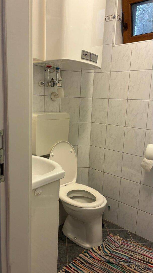 Kleines WC mit Fliesenwänden, Toilette, Waschbecken und Fenster für natürliche Belüftung.