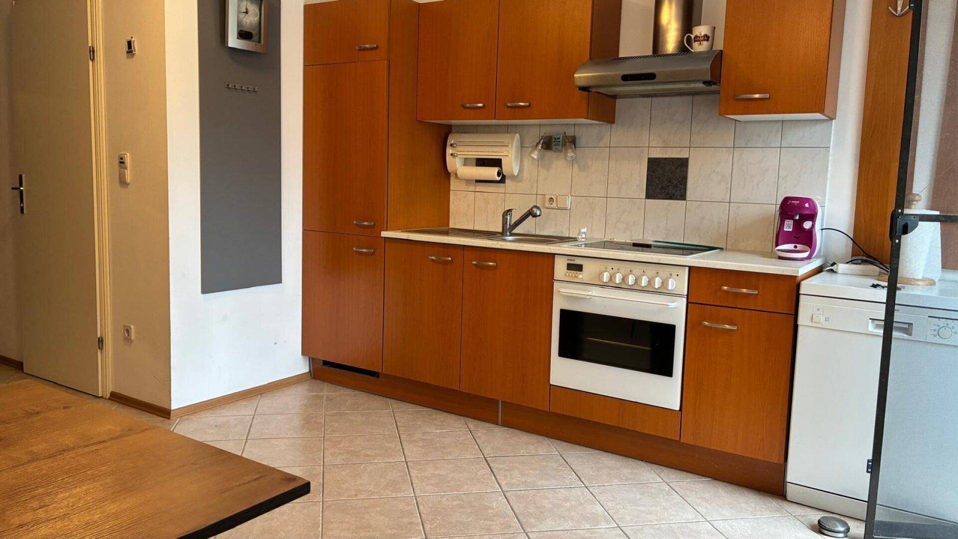 Gut ausgestattete Küche mit braunen Holzfronten, integrierten Geräten und Fliesenboden.