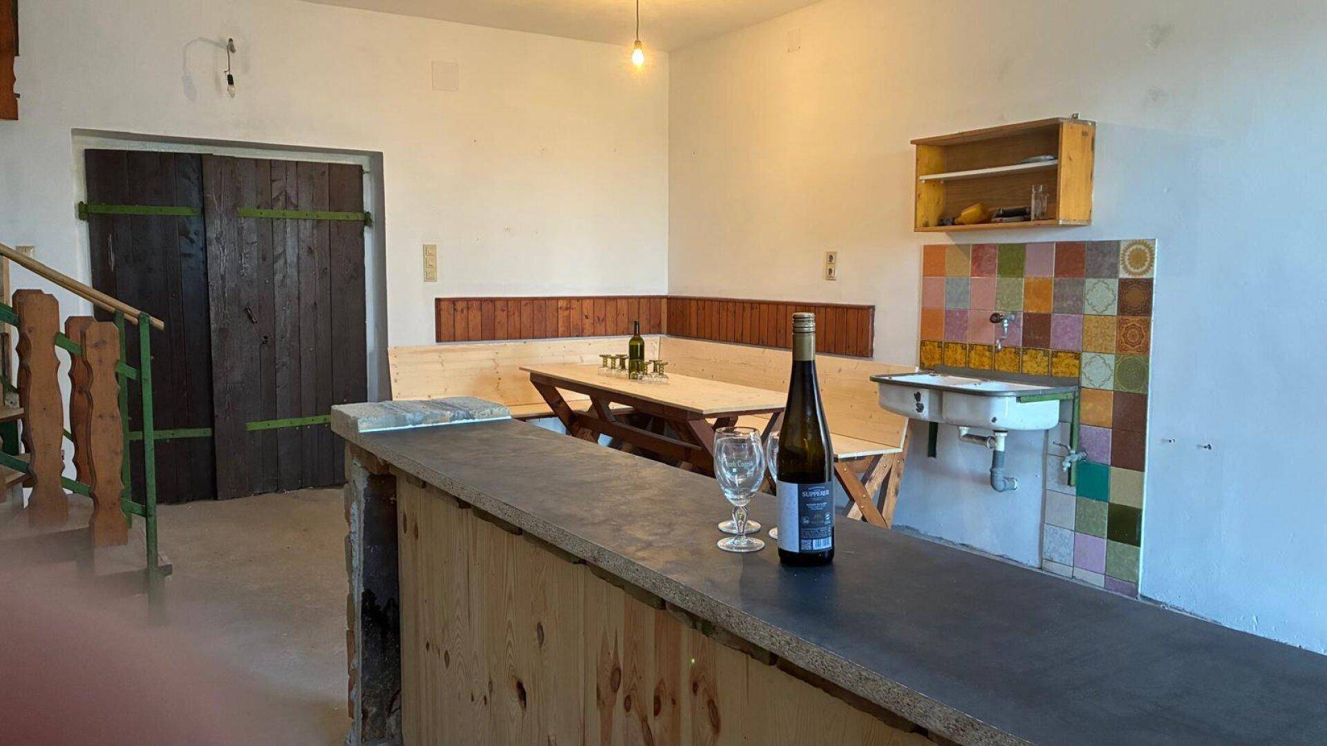 Gemütlicher Raum mit Holzbänken, Tisch und einer Bar, perfekt für Weinproben.