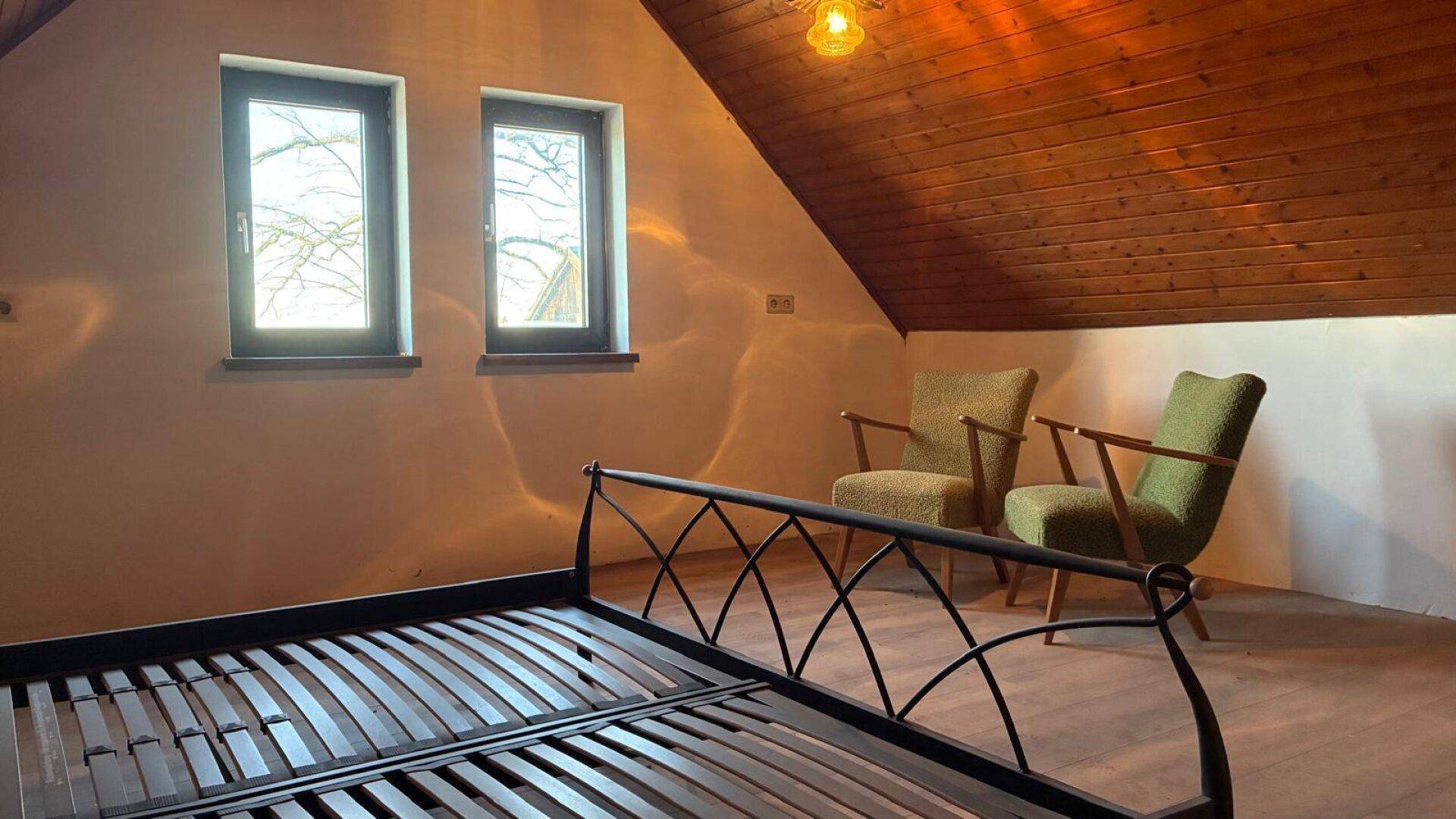 Helles Schlafzimmer im Dachgeschoss mit Holzbalkendecke und zwei Fenstern.