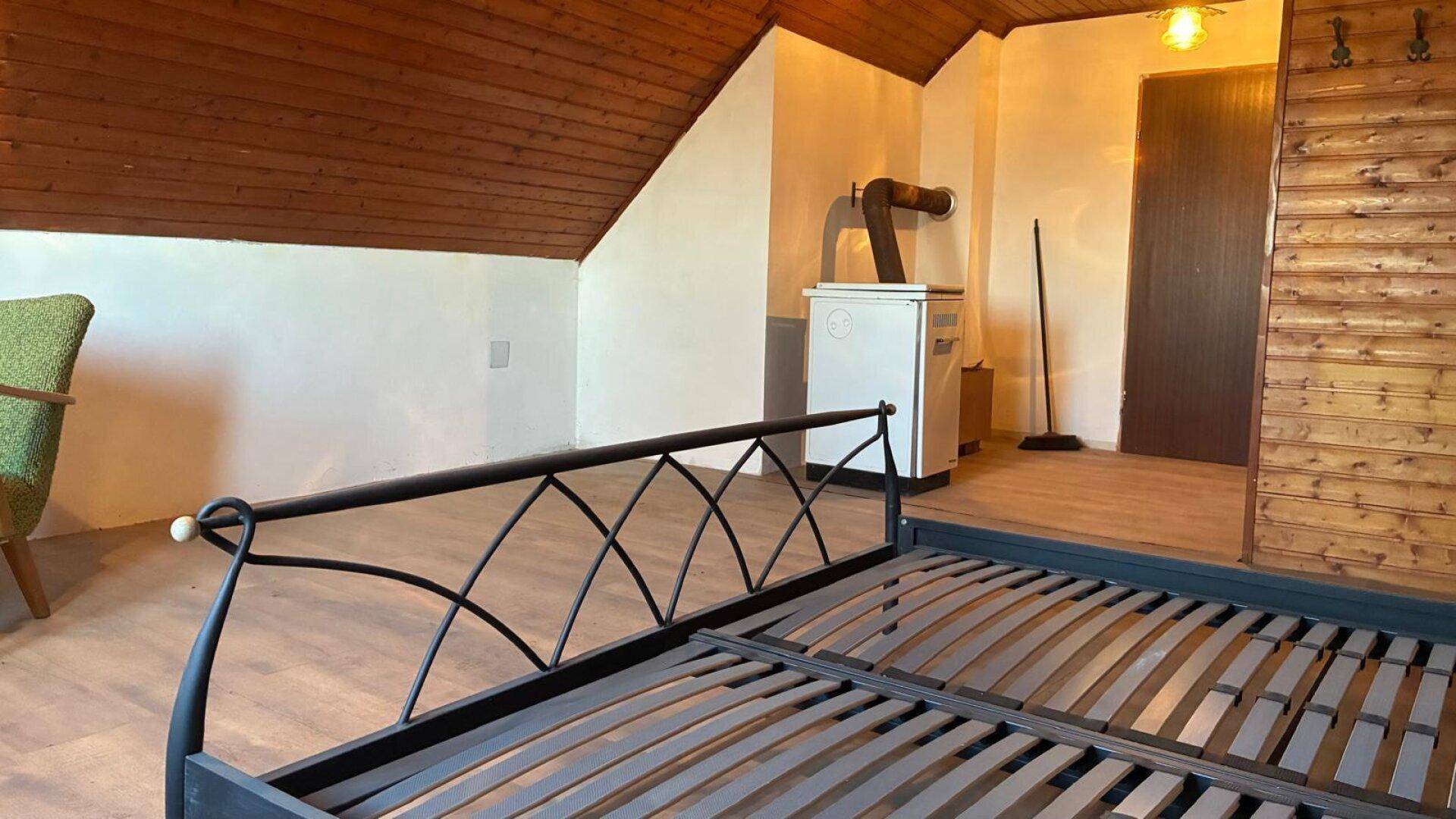 Schlafzimmer im Dachgeschoss mit Holzbalkendecke und einem Holzofen für Wärme.
