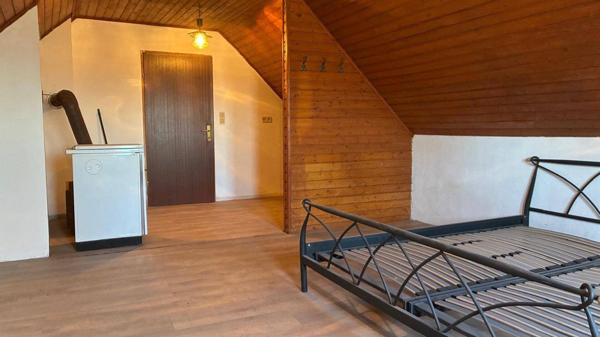 Dachgeschoss-Schlafzimmer mit Holzbalkendecke, Holzwandverkleidung und Zugang zu einem weiteren Raum.