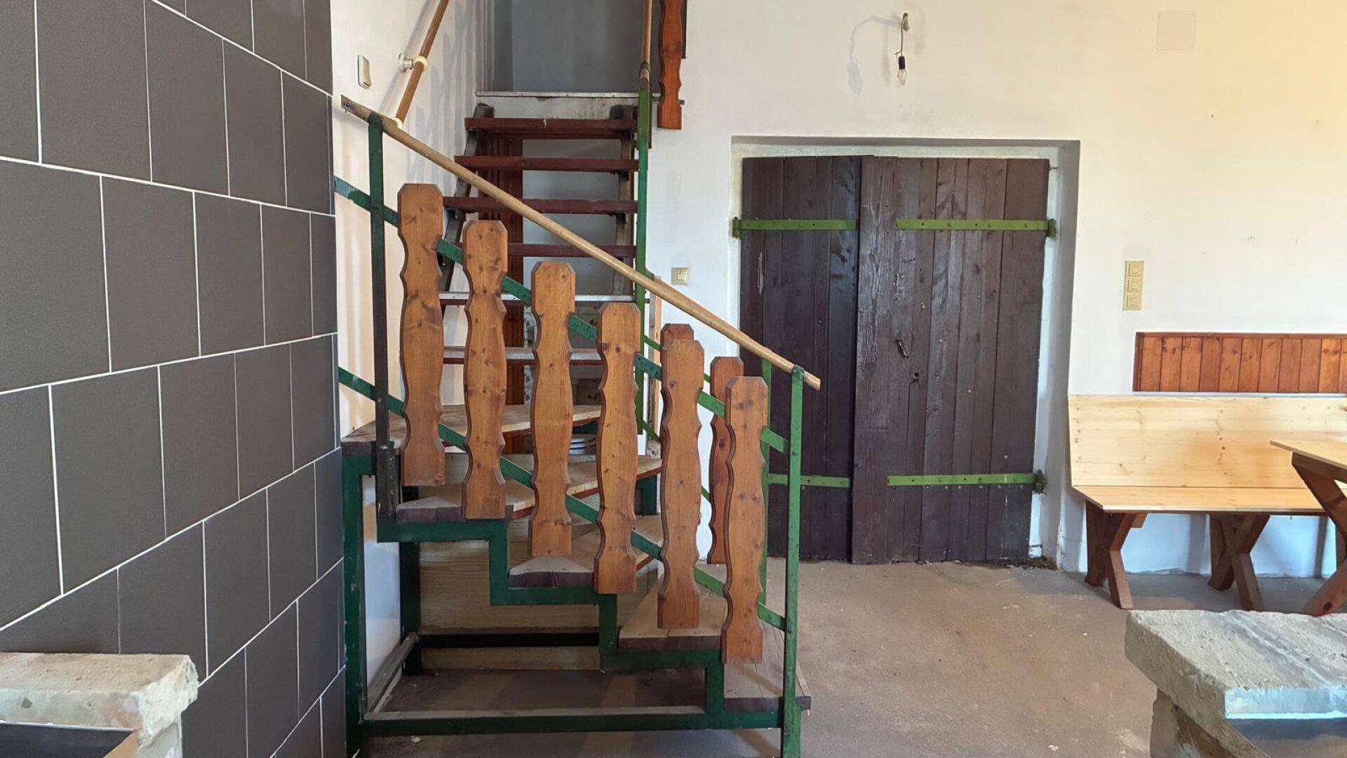 Rustikales Treppenhaus mit Holzgeländer und gefliestem Bereich im Eingangsbereich.