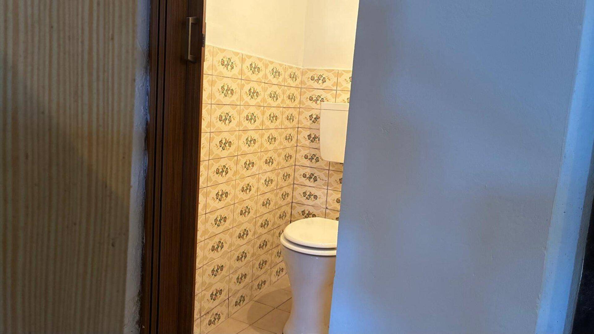 Einfaches WC mit gemusterten Fliesen an den Wänden und auf dem Boden.