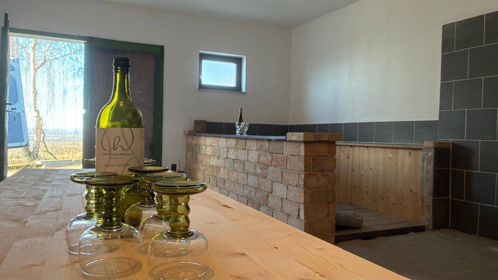 Rustikaler Raum mit Holztisch, gemauertem Tresen und Blick ins Grüne durch die Tür.