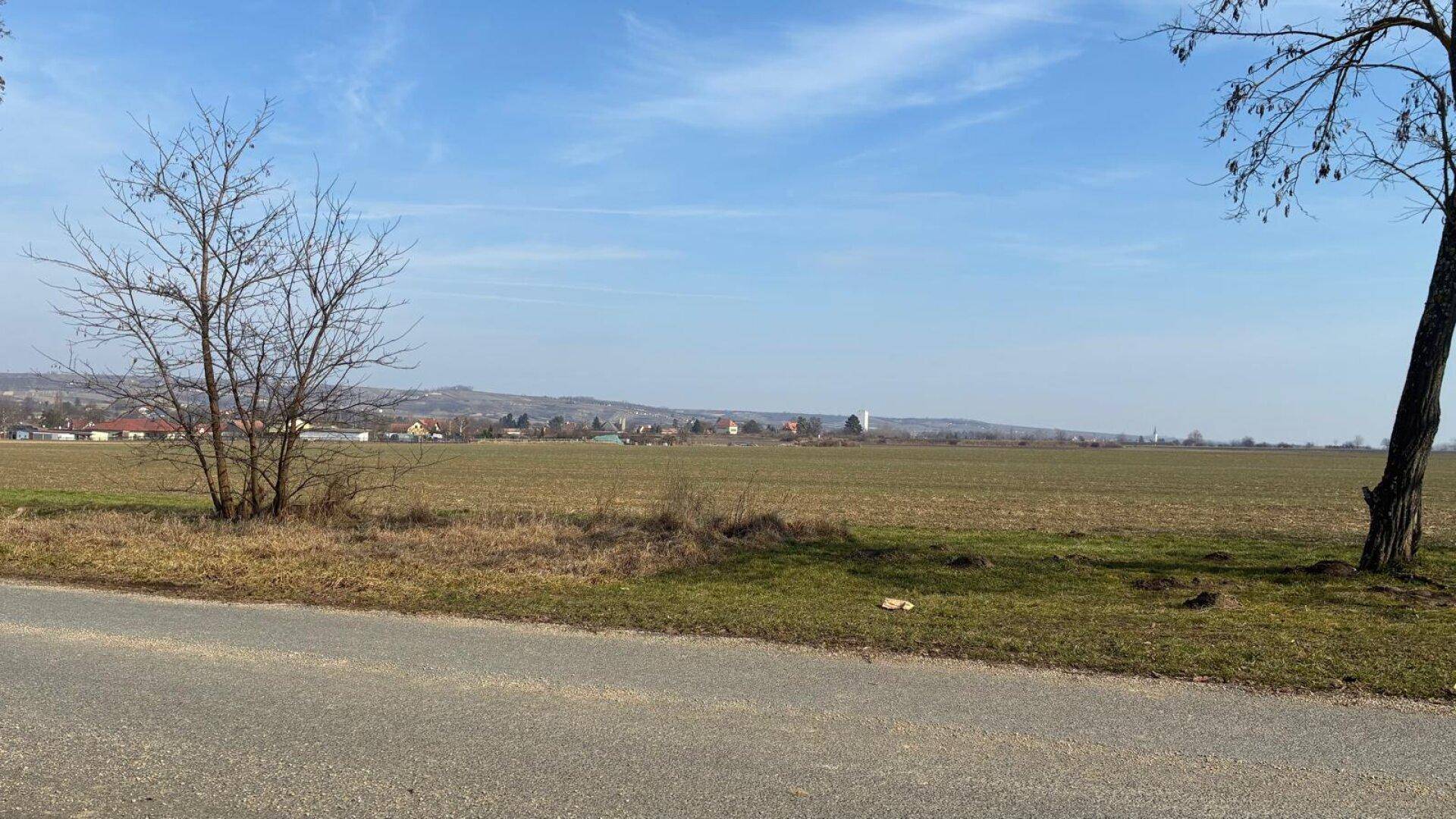 Weite Felder und ländliche Landschaft mit vereinzelten Häusern am Horizont unter klarem Himmel.