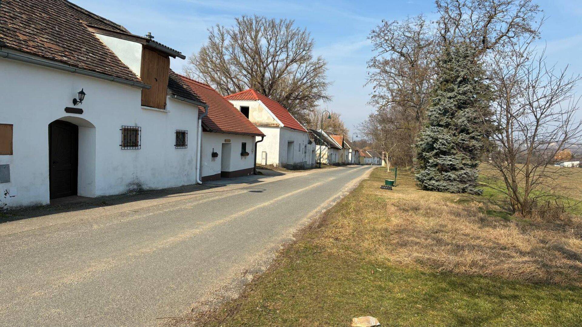 Reihe alter, weiß getünchter Gebäude mit Ziegeldächern entlang einer ländlichen Straße.