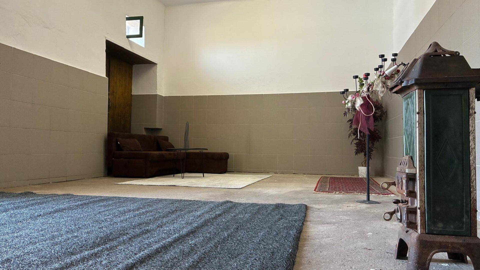 Großer, heller Raum mit Betonboden, einem Ofen und Teppichen, ideal für Umgestaltung.